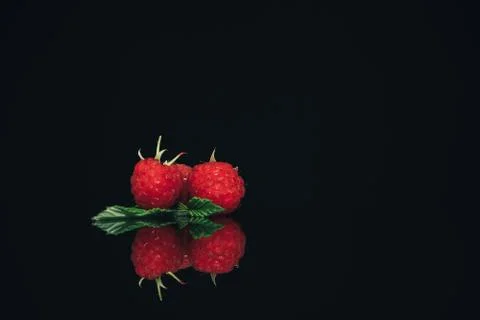 Beautiful three fresh raspberry on a black glass table dark background. Foto stock