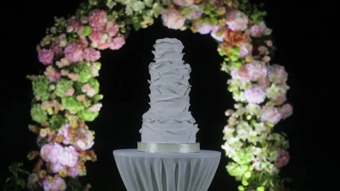 A beautiful three-tier all white wedding cake on a table under an arch in the Stock Footage 280169999