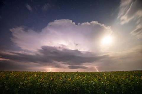 Beautiful thunderstorm with clouds, lightning and moon over a field Stock Photos