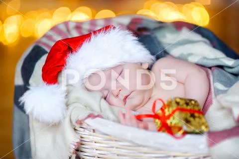 Beautiful toddler in a Santa Claus hat holds a gift hand and sleeps in a bask Stock Photos