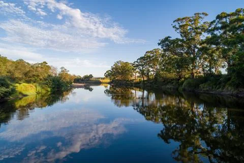 Beautiful tree reflections in calm river at sunset Stock Photos