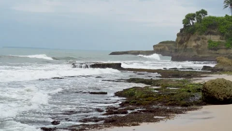 Beautiful tropical beach with rocky cliffs, white sand, and ocean waves. Stock Footage 329782895