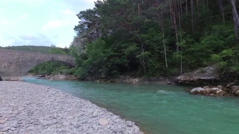 A beautiful turquoise river flows under a bridge in the mountainous regions of P Stock Footage 94337697