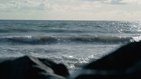 Beautiful view of slow motion waves behind out of focus rocks on beach Stock Footage 119533392