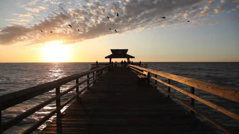 Beautiful view of a sunset over a pier, birds flying over the ocean Stockbeeldmateriaal 276609492