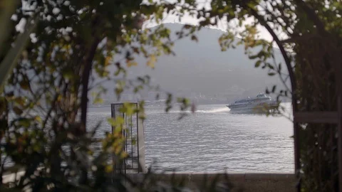 Beautiful view through an arch of plants as a hydrofoil boat floats on Lake Como Stock Footage 128748252
