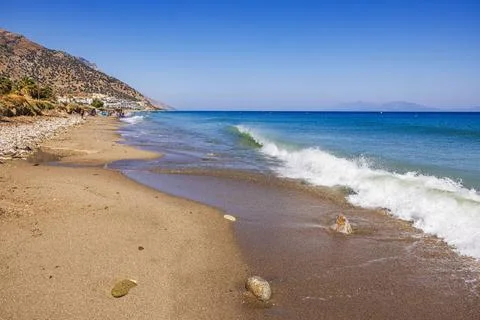 Beautiful view of waves on pebble beach Aegean sea on blue sky background. Stock Photos