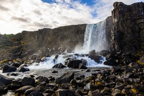 Beautiful waterfall with black rocks on the surface on a sunny day. Stock Photos