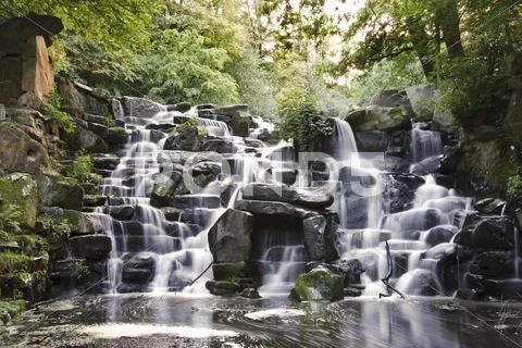 Beautiful waterfall cascades over rocks in lush forest landscape Stock Photos