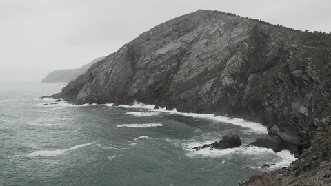 Beautiful waves hit the rocks of a large cape. Cloudy weather. Seagulls fly over Stock Footage 121614436