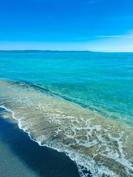 Beautiful waves roll onto a sandy beach under clear blue skies during the d.. Stock Photos