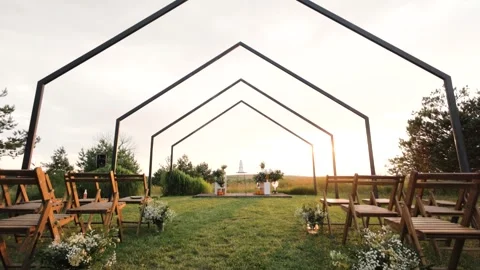A beautiful wedding cake on a table under an arch in a field at sunset. Full Stock Footage 279771768