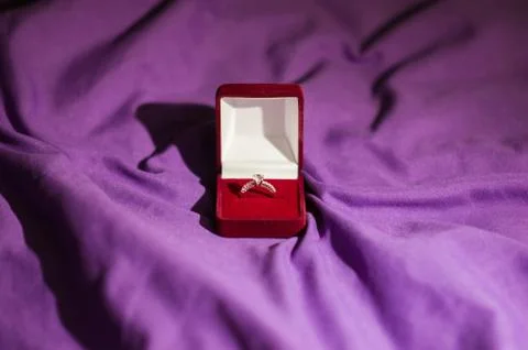 Beautiful wedding ring with precious stone in red velvet gift box on violet b Foto stock