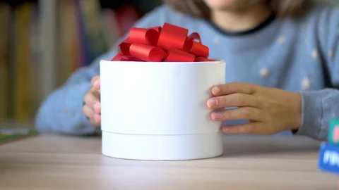 Beautiful white box with a red bow in the hands of a child. A little girl opens Stock Footage 126770604