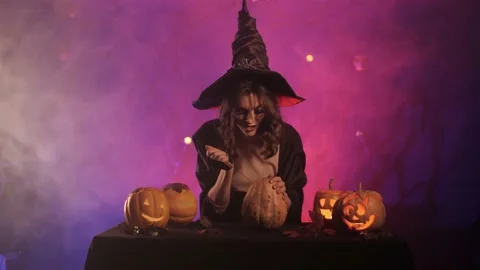 Beautiful witch laughs and cuts a pumpkin for halloween Stock Footage 163752377