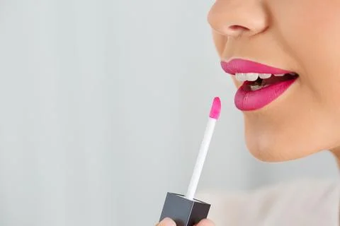 Beautiful woman applying liquid lipstick on light background, closeup. Space  Stock Photos