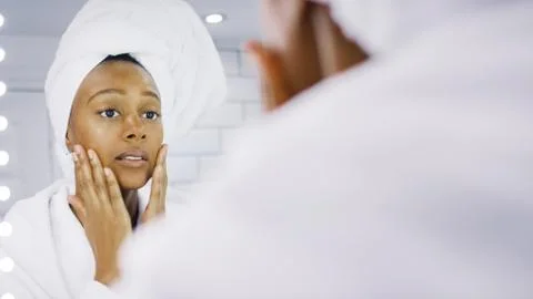 Beautiful woman applying moisturiser to her face in front of the bathroom mirror Stock Photos