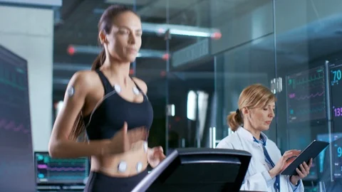 Beautiful Woman Athlete Runs on a Treadmill with Electrodes Attached to Her Body Stock Footage
