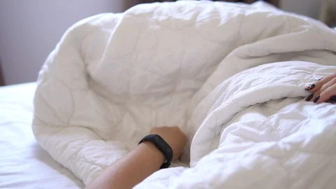 Beautiful woman checking data on her fitness tracker band after waking up in the Stock Footage 91657419