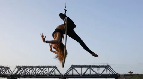 Beautiful woman doing acrobatic elements on aerial hoop hanging on a bridge Stock Footage 64598509