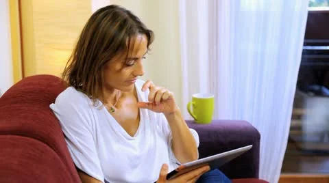Beautiful woman drinking tea at home while reading tablet Stock Footage