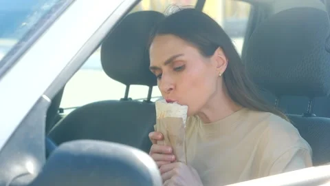 Beautiful woman driver eats shawarma in car when greasy food piece falls on t Stock Footage 312847177