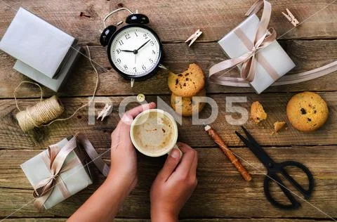 Beautiful woman hands holding gift box on wooden background. Black alarm clock Stock Photos