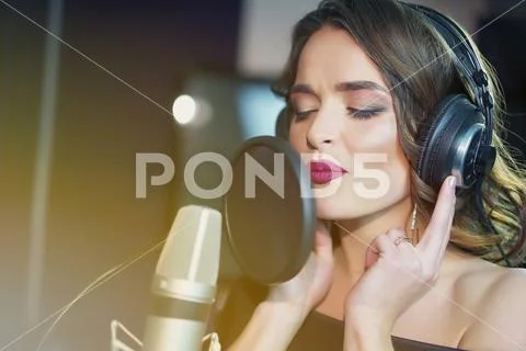 Beautiful woman in headphones records a song in a professional recording stud Stock Photos