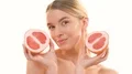 The beautiful woman holding two halves of a grapefruit on the white background 4k or 4k+ Resolution