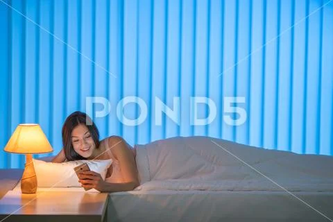 The beautiful woman lay on the bed and phone. Evening night time Stock Photos