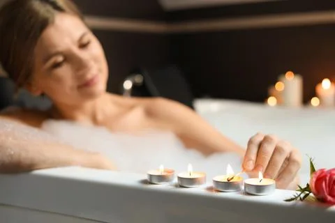 Beautiful woman lighting candles while taking bubble bath, focus on hand. Rom Stock Photos
