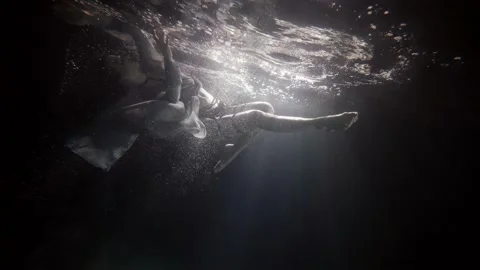 A beautiful woman in a long dress hovers on her back under the water on a dark Stock Footage