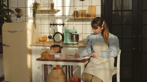 Beautiful woman is making notes while cooking in the kitchen. Stock Footage 125827142
