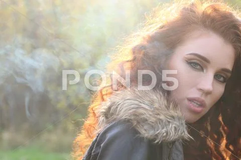 Beautiful woman with red hair in jacket among smoke in sunshine, shallow dof Stock Photos