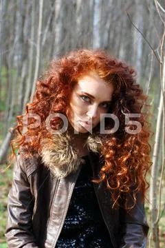 Beautiful woman with red hair in leather jacket poses in sunny autumn forest Stock Photos