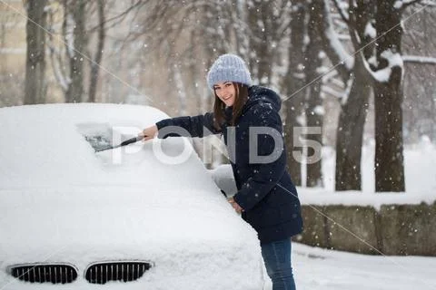 Beautiful woman removing snow from car windshield. Stock Photos