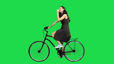 A Beautiful woman riding a bicycle over a green screen, looking around. Stock Footage