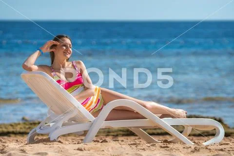 The beautiful woman sit on the sunbed on the sea background Stock Photos