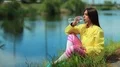 Beautiful woman sits on the grass near the lake and drinks water HD Footage