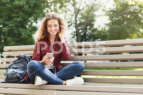 Beautiful woman sitting and listening music on the smartphone outdoors Stock-Fotos