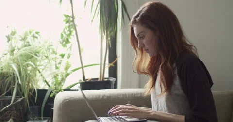 Beautiful woman sitting on couch using laptop in living room Vídeo Stock 63374264
