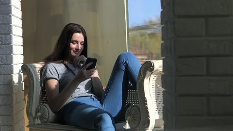 Beautiful woman sitting on sofa and looking out the wide window phone Stock Footage