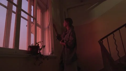 A beautiful woman standing near window can see cityscape at Sunset in Moscow Stock Footage