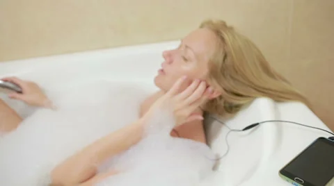 Beautiful woman taking a bath and listening to music on headphones. cell phone Stock Footage