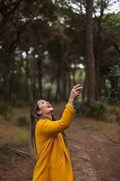 Beautiful woman throwing her hat in the air with a yellow coat in nature. Smi Stock Photos