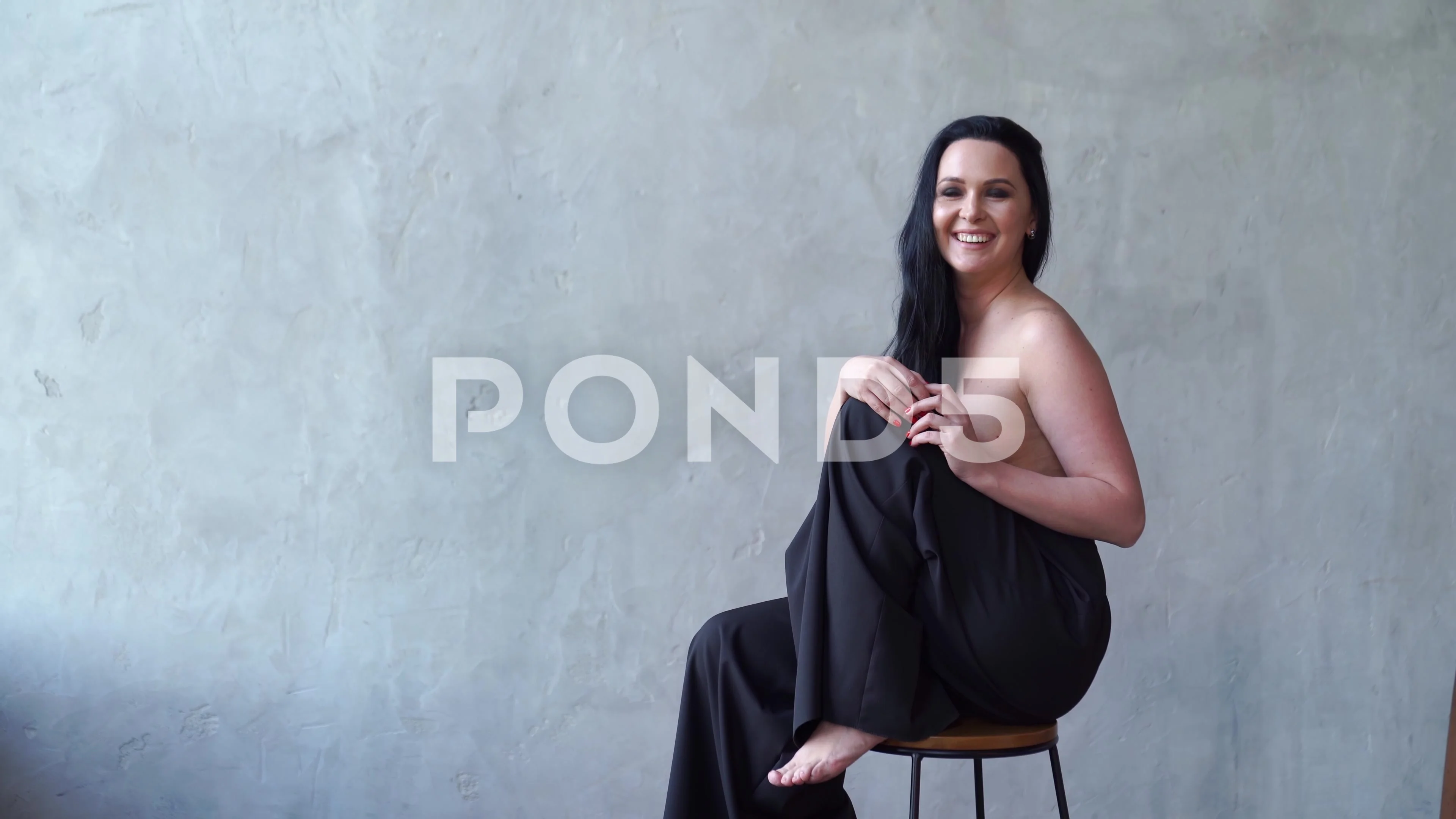 A beautiful woman topless sitting on a high chair.