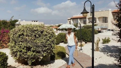 Beautiful woman with umbrella walks at the territory of the hotel Stock Footage