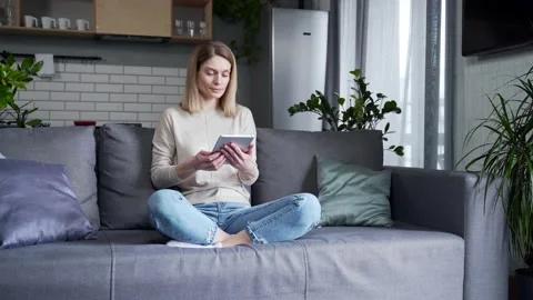 Beautiful woman uses a tablet while sitting on the sofa in the living room  Stock Footage 231224275