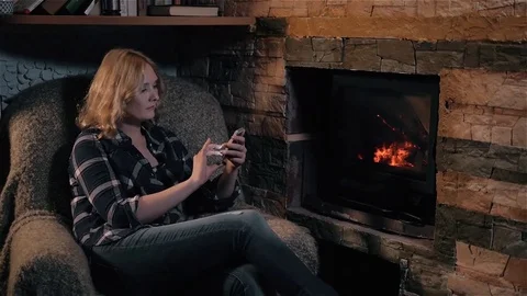 Beautiful Woman Using Smartphone Sitting By Fireplace at Home, Holiday And Stock Footage 72139146