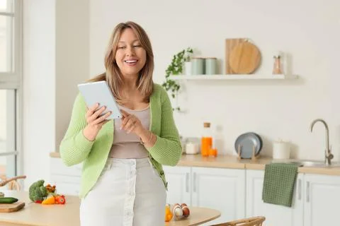 Beautiful woman using tablet computer in kitchen Stock Photos